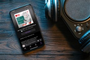 Podcast Ein Handy mit einer Podcastfolge zum Thema Kopfläuse ist zu sehen. Neben dem Handy liegen Kopfhörer am Tisch