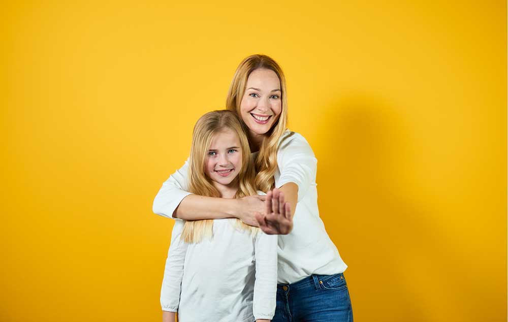 Läuse-Befall Eine Mutter umarmt Ihre Tochter vor einem gelben Hintergrund