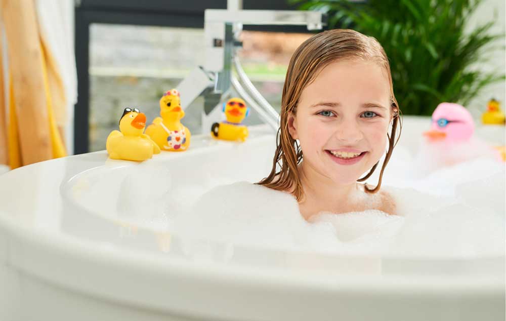 Mosquito Läuse Shampoo Ein Mädchen sitzt in einer Badewanne und hinter ihr stehen gelbe Quietscheenten