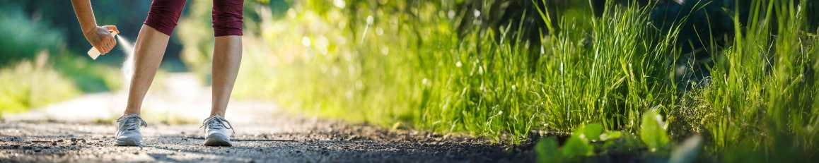 Woman spraying insect repellent against mosquito and tick on her leg before jogging in nature