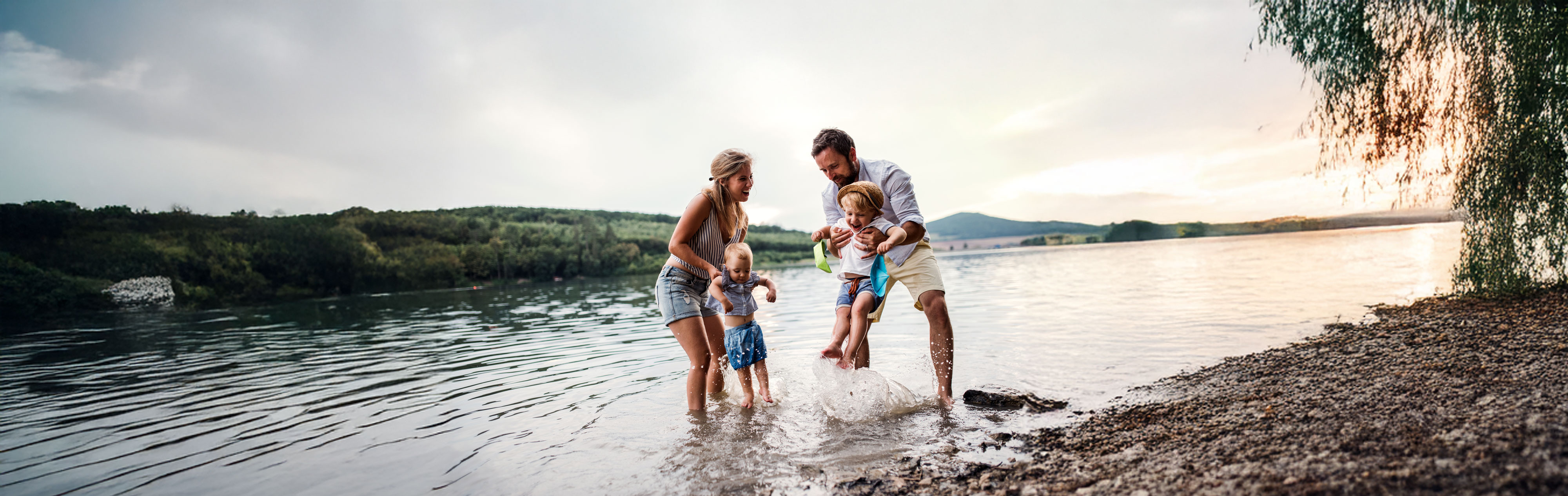A young family with two toddler children outdoors by the river in summer.